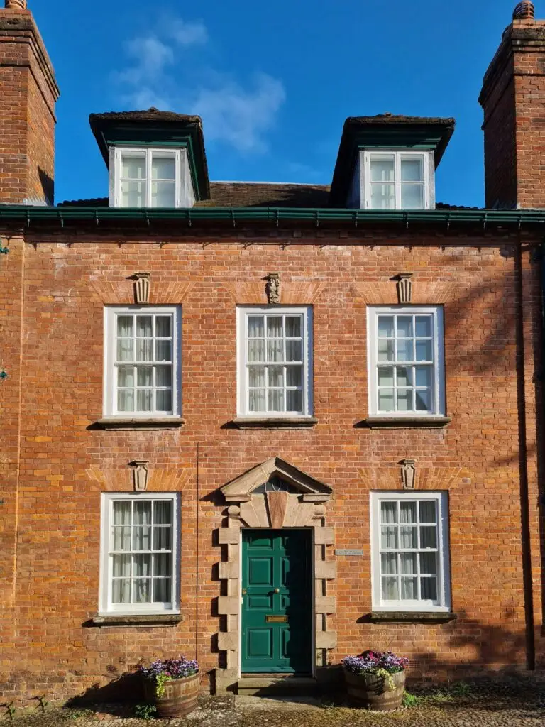 A classic red brick facade with green door in Ledbury under a clear blue sky.